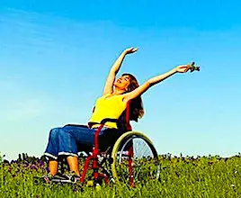 Une jeune femme en fauteuil roulant, dans un champ, qui lève les bras au ciel. En avril, le secteur du handitourisme va mieux se faire connaître.