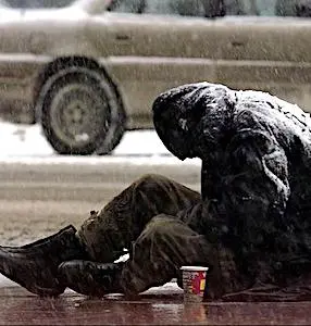 Une personne sans-abri qui mendie sur un trottoir, par temps de neige. Dans certaines régions, le Plan Grand Froid est une nécessité fréquente en hiver.