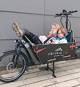 Deux enfants dans un caisson de vélo-cargo Les vélos-cargos urbains deviennent un moyen familial de locomotion qui s’intensifie.