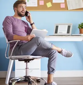 Un télétravailleur assis chez lui, devant son bureau. Les changements dus au télétravail concernent à la fois le matériel informatique et les comportements professionnels.