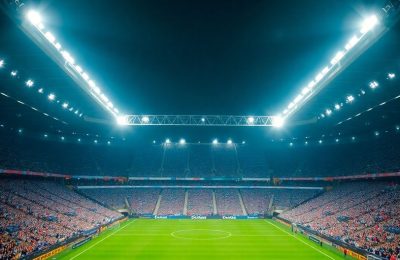 Stade de Premier League avec des fans, sous les projecteurs.
