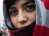 Femme iranienne voilée, regard déterminé, foule en arrière-plan.