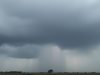 Nuages sombres et pluie tombant sur un paysage rural.