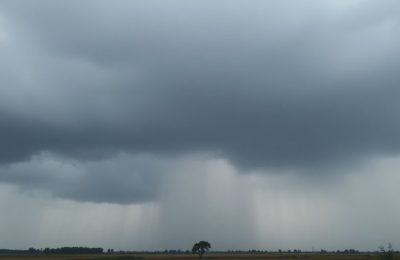 Nuages sombres et pluie tombant sur un paysage rural.