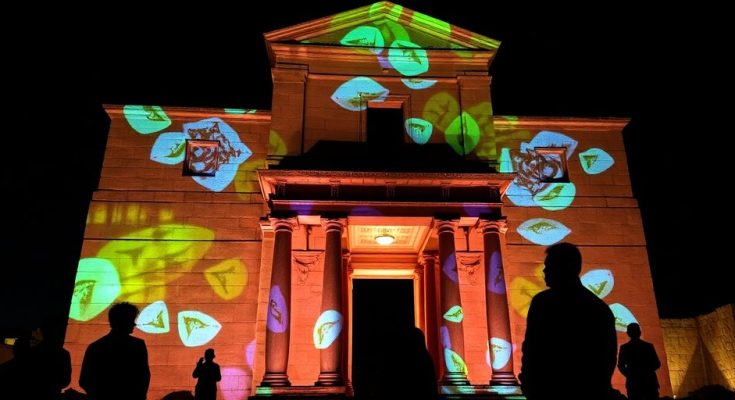 Monument historique illuminé par des projections lumineuses, entouré de visiteurs.