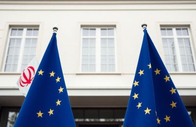 Drapeaux de l'Iran et de l'Europe près d'un bâtiment officiel.