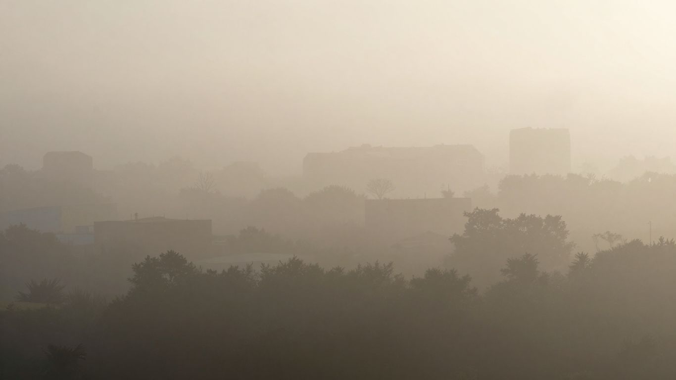 Paysage brumeux avec des formes indistinctes de bâtiments et d'arbres.