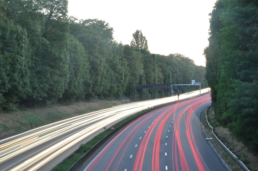 Vacances de la Toussaint 2026 : traînées lumineuses de voitures sur une route bordée d'arbres au crépuscule